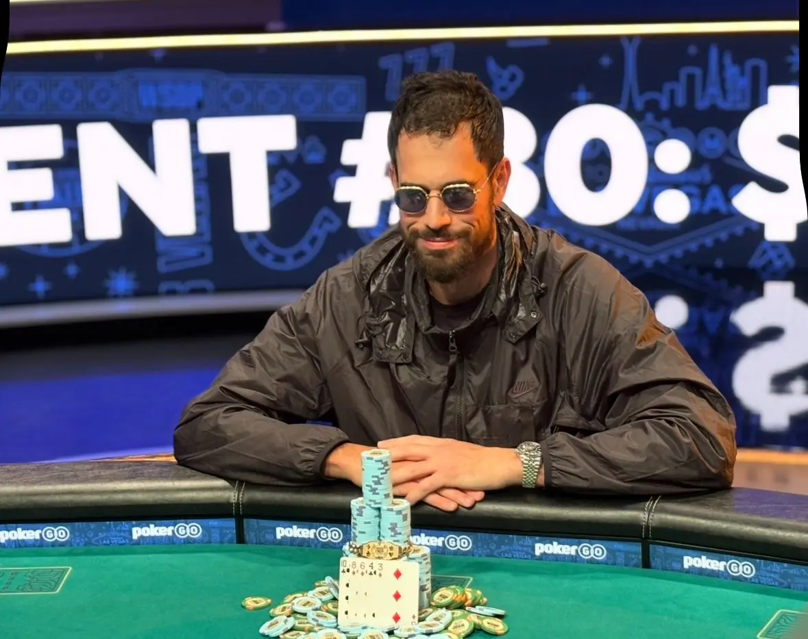 Nick Schulman mit Sonnenbrille und schwarzer Jacke an einem Pokertisch mit Pokerchips.