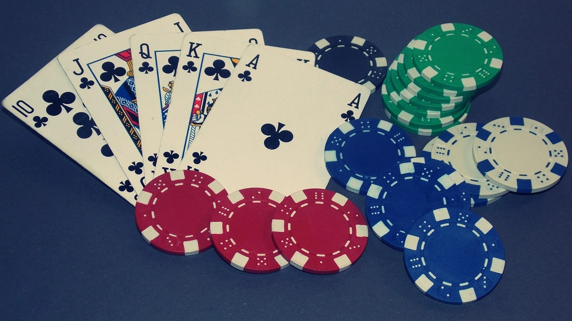 Ein Royal Flush in Herz sowie verschiedene Pokerchips auf einem blauen Hintergrund.
