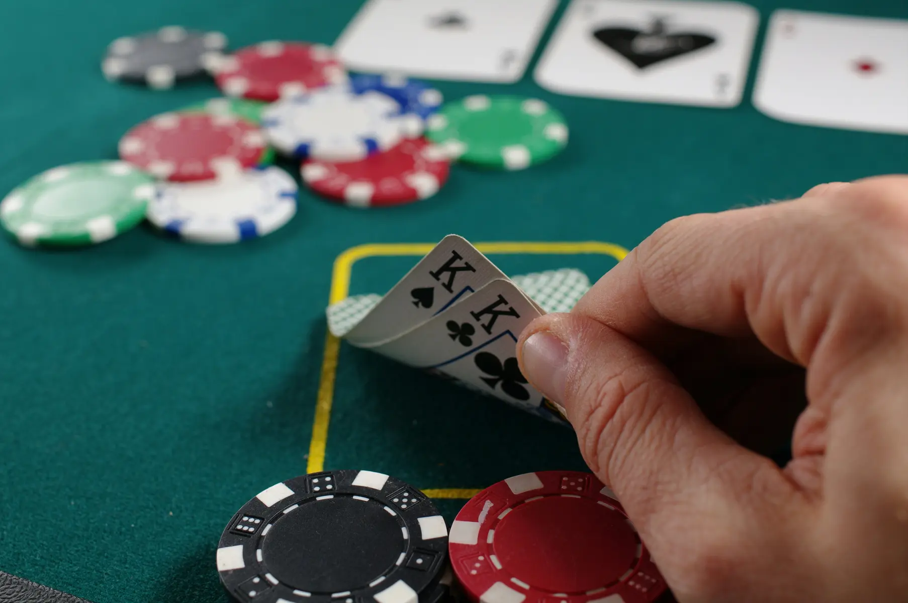 Eine Hand hält zwei Könige auf einem grünen Pokertisch mit Spielchips und Karten.