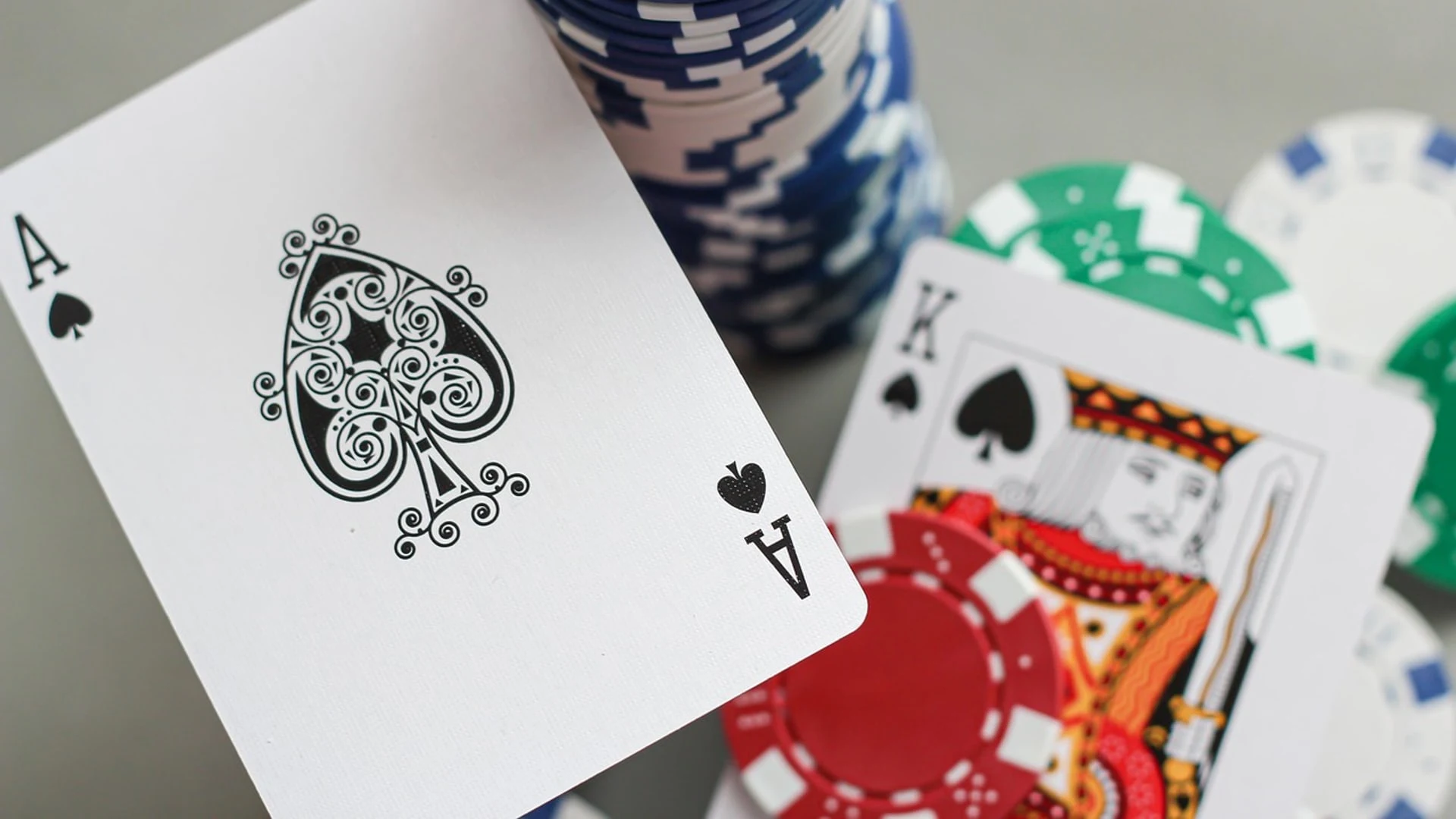 Pokerchips und Spielkarten auf einem Tisch, darunter ein Pik-Ass.
